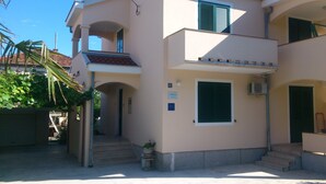 A two-story building with a balcony, a small staircase leading to the entrance, and a potted plant near the door. - Apartments Aurora (Zadar)