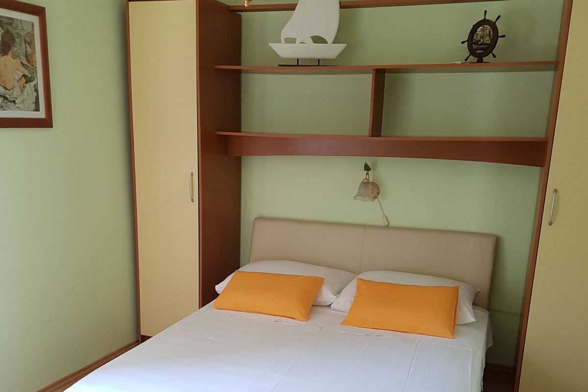 A bed with white and orange bedding, a wooden headboard, and a shelf with decorative items.