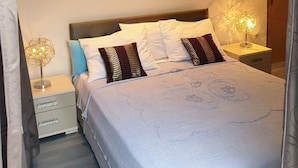 A neatly made bed with a white comforter and patterned pillows, a bedside table with a lamp, and two framed pictures on the wall. - Apartments Aurora (Zadar)
