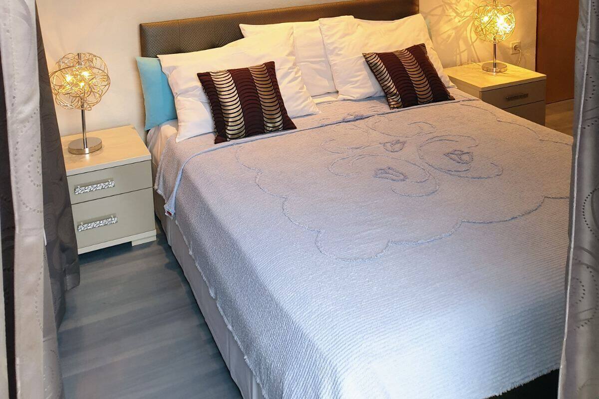 A neatly made bed with a white comforter and patterned pillows, a bedside table with a lamp, and two framed pictures on the wall.