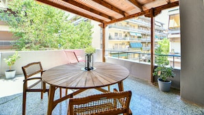 A wooden table and chairs on a balcony with potted plants, overlooking a residential area with balconies and buildings. - Flowers Of Athens - Boutique Aparthotel (Athens)