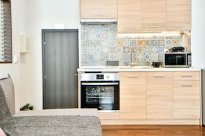 A compact kitchen with wooden cabinets, a microwave, and a built-in oven. - Flowers Of Athens - Boutique Aparthotel (Athens)