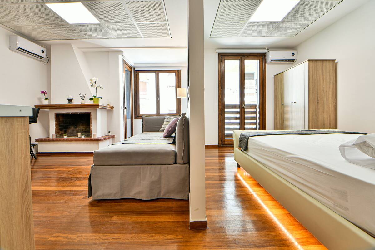 Ein modernes Hotelzimmer mit Holzboden, einem Bett, einer Couch, einem Kamin und einem großen Fenster.