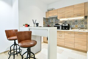 A modern kitchen with two bar stools, wooden cabinets, and a tiled backsplash. - Flowers Of Athens - Boutique Aparthotel (Athens)
