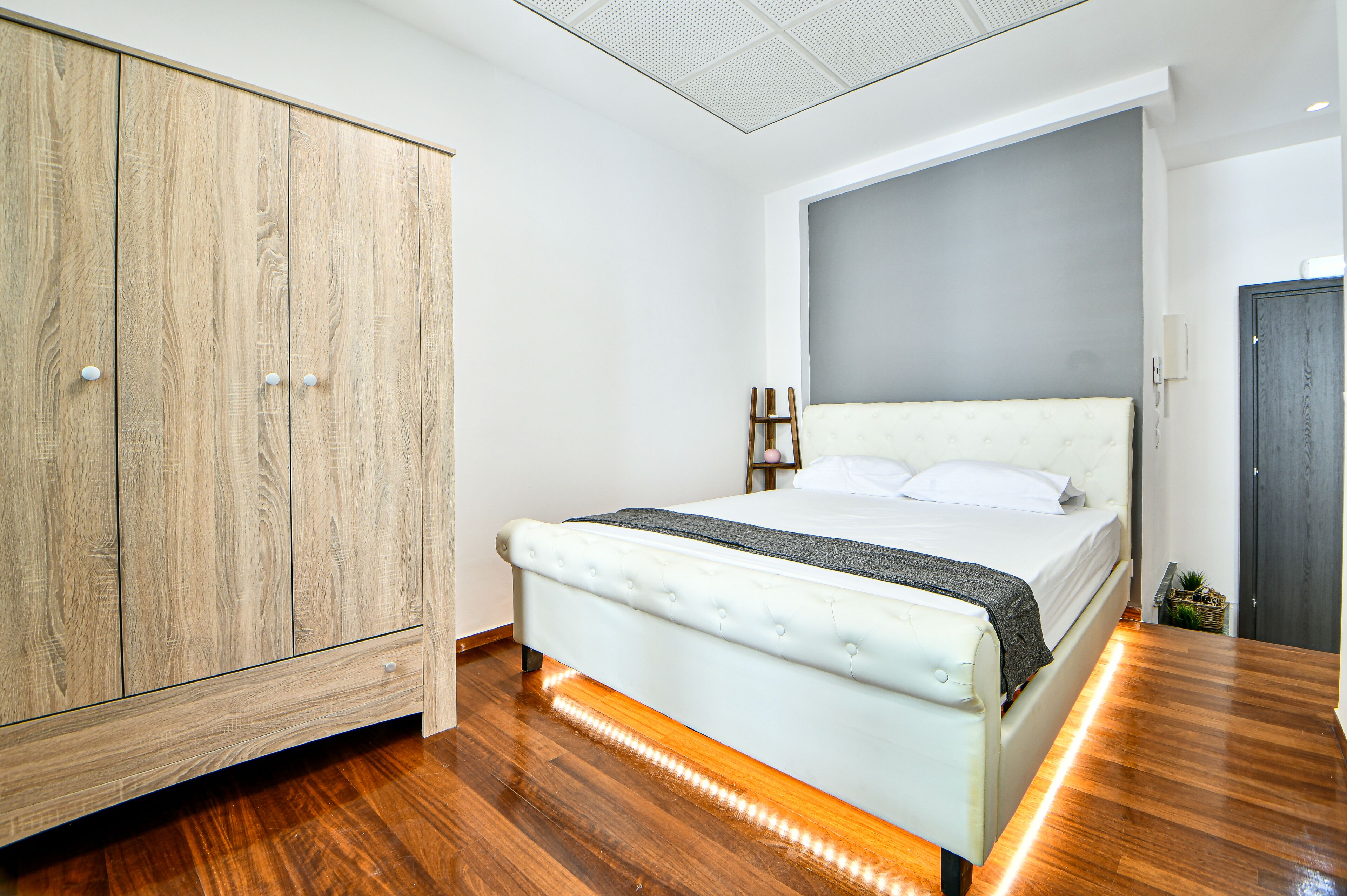 Un dormitorio con un armario de madera, una cama con cabecera blanca y una pared de acento gris.