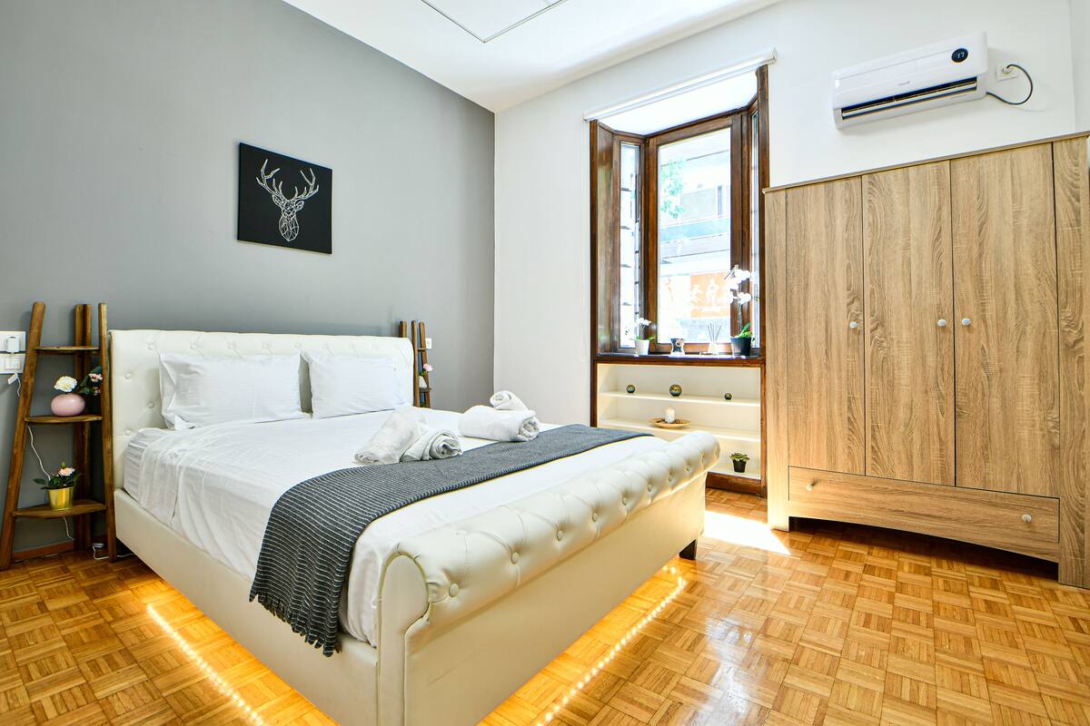 Ein ordentlich eingerichtetes Schlafzimmer mit Bett, Kleiderschrank, Fenster und einer Wand-Klimaanlage.