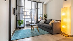 Una sala de estar moderna con un sofá gris, una mesita redonda pequeña, un tapete azul y una lámpara de pie grande.