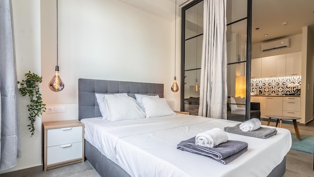 A modern hotel room with a large bed, bedside tables, a desk, and a view of the kitchen. - Plenty Apartments Zeus (Athens)