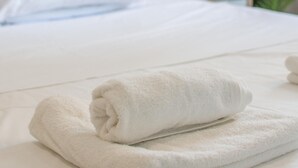 Een net opgemaakt bed met witte lakens en een opgevouwen witte handdoek op de zijkant.