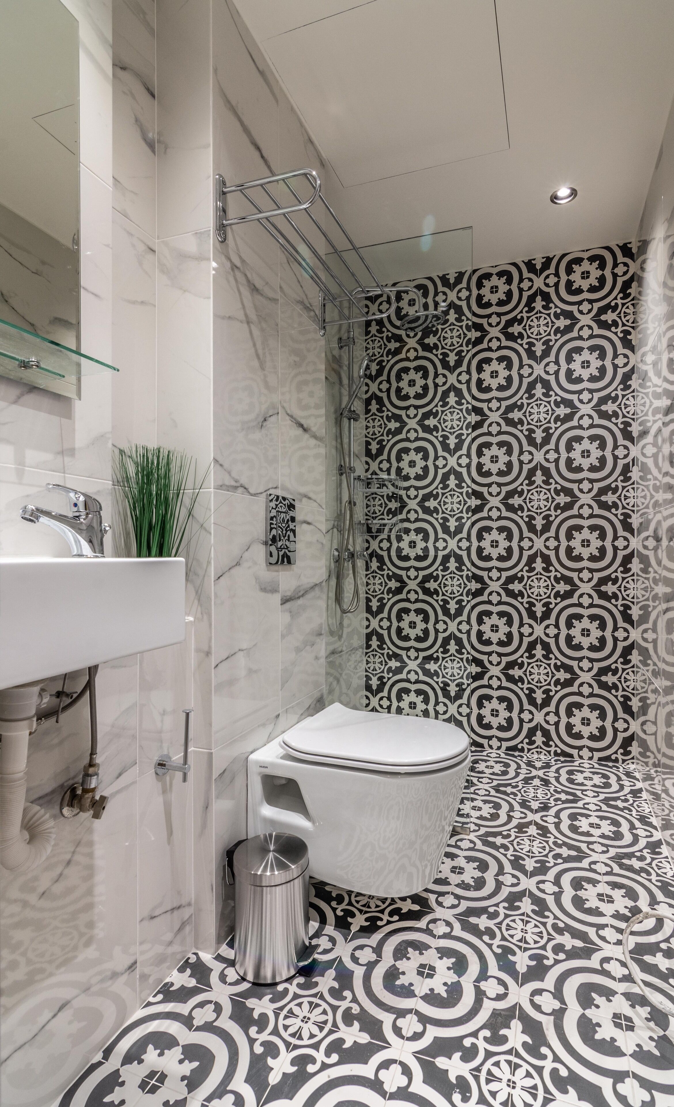 A modern bathroom with a marble sink, a toilet, and a shower with patterned tiles.