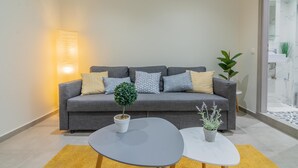 Moderni olohuone, jossa on harmaa sohva, pyöreä sohvapöytä ja ruukussa oleva kasvi.