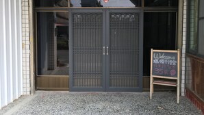 A building entrance with a large metal gate, a small signboard, and a tiled ground. - Reui Heng Guesthouse (Budai)