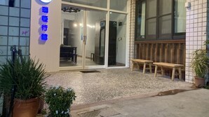 A building with a glass door entrance, a sign with Chinese characters, and two wooden benches outside. - Reui Heng Guesthouse (Budai)