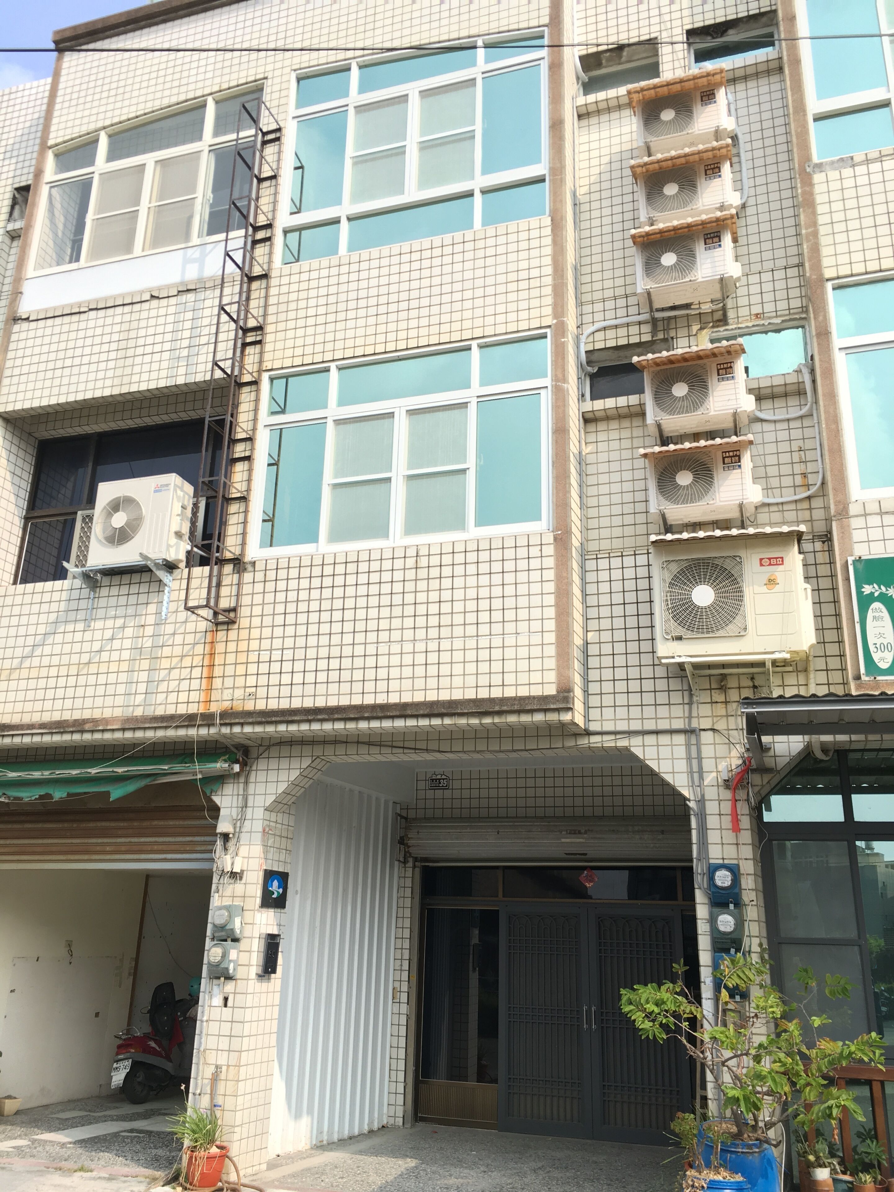 A multi-story building with tiled exterior walls, multiple air conditioning units, and a gated entrance.