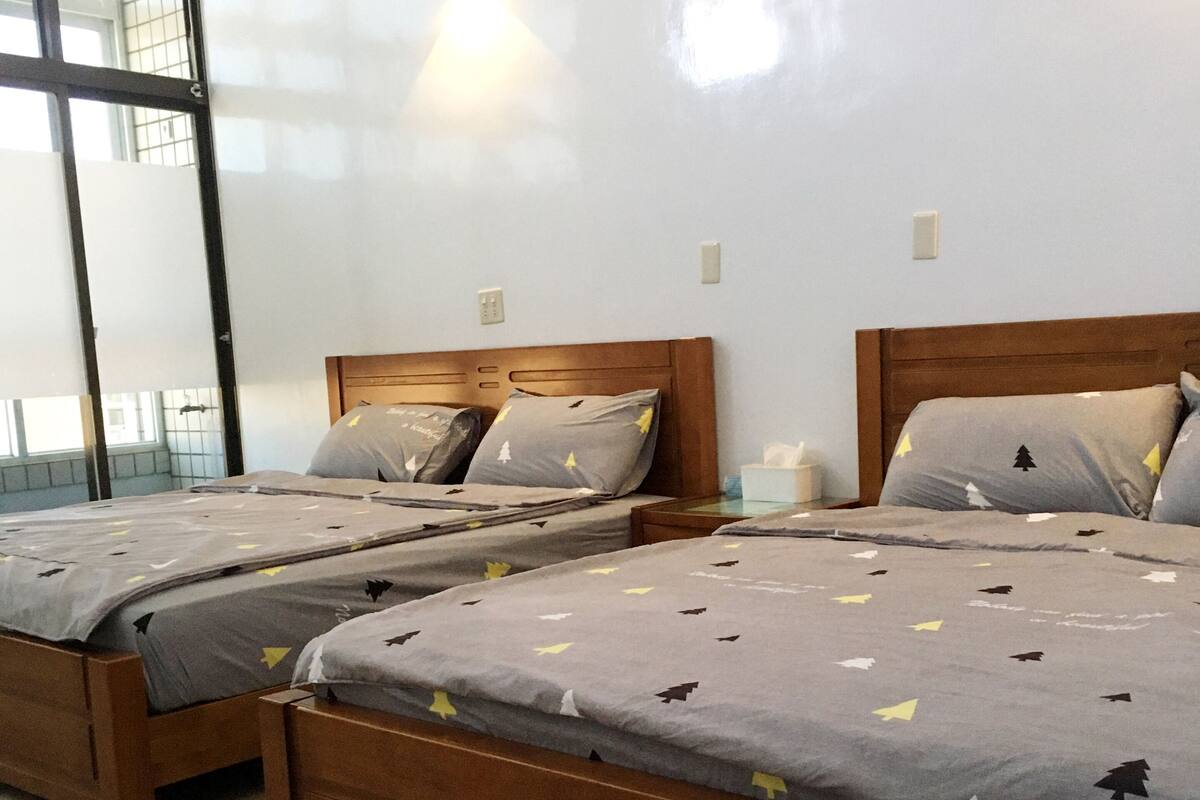 A hotel room with two wooden beds, a large window, and a wall-mounted light fixture.