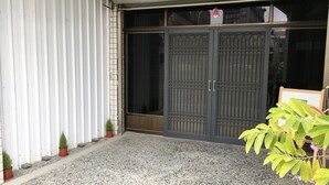 A building entrance with a closed metal gate, potted plants, and a gravel driveway. - Reui Heng Guesthouse (Budai)