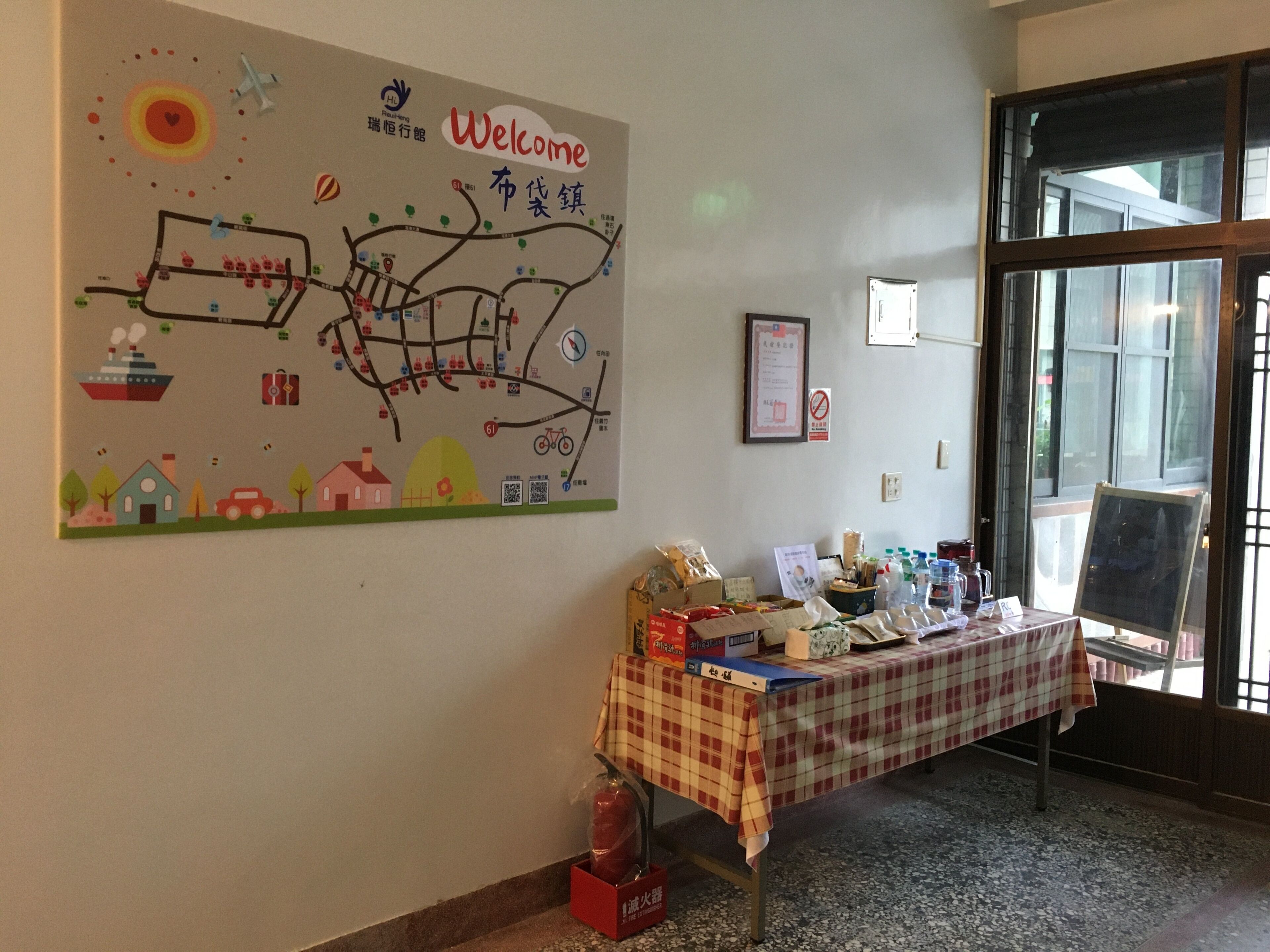 A room with a large welcome map on the wall, a table with various items, and a door leading outside.