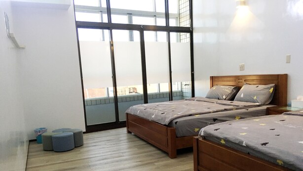 A modern bedroom with two wooden beds, a large window, and a balcony. - Reui Heng Guesthouse (Budai)