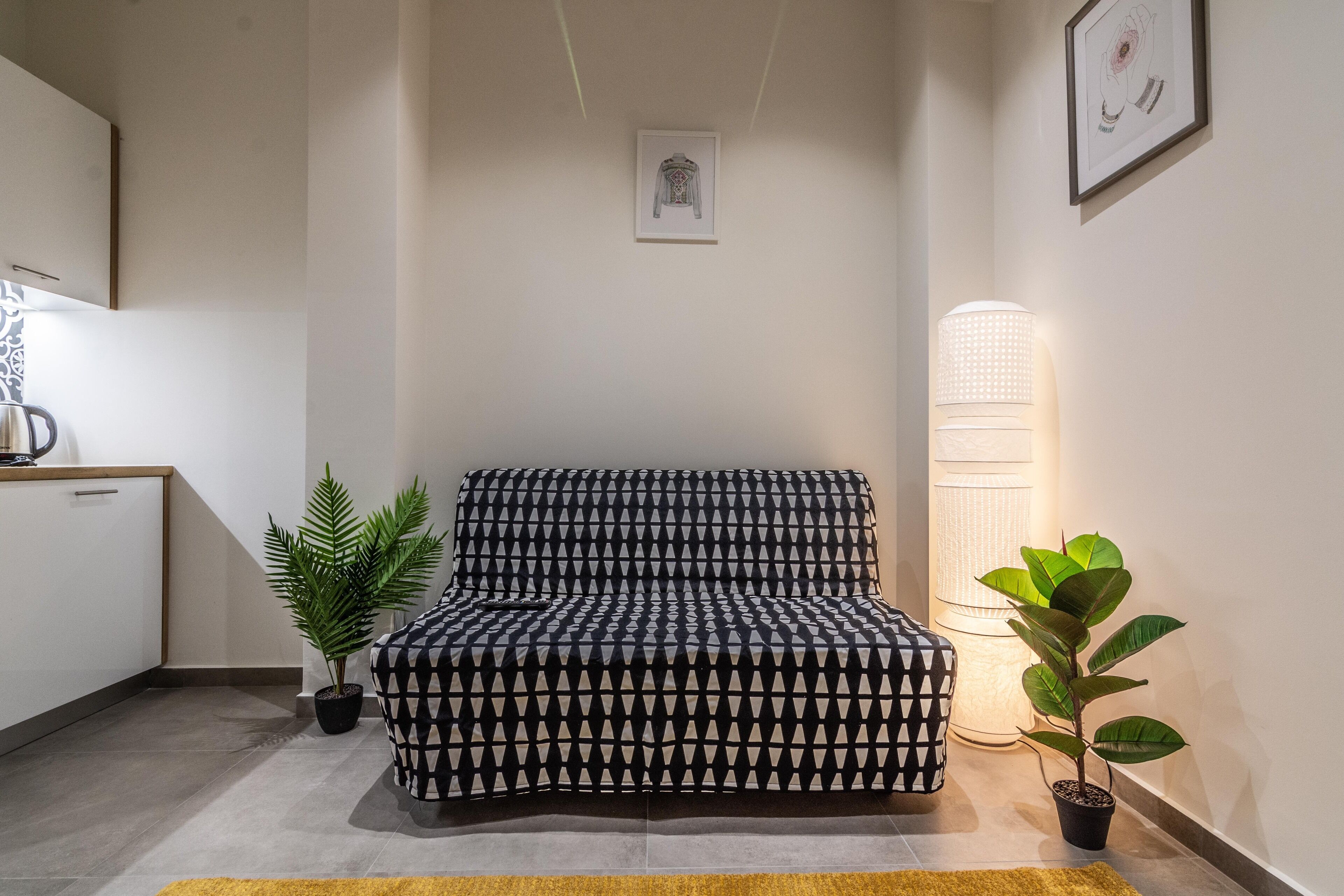 Een moderne woonkamer met een gestreept bankje, een potplant, een vloerlamp en een ingelijst schilderij aan de muur.