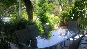 A glass-top table with four chairs, surrounded by lush greenery and potted plants. - Historic Inn Vacation Rental (Ashfield Colborne Wawanosh)