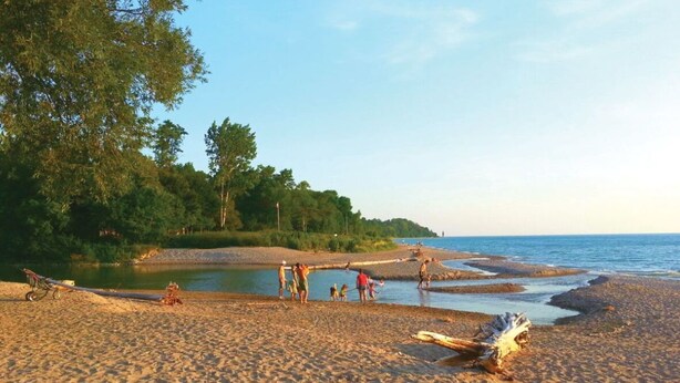 A sandy beach with people and a bicycle, trees in the background, and a calm sea. - Historic Inn Vacation Rental (Ashfield Colborne Wawanosh)
