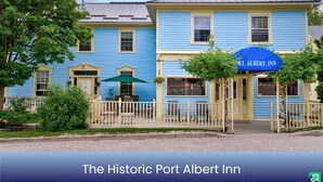 The Historic Port Albert Inn with a traditional architectural style, featuring a prominent entrance with a blue awning and a white picket fence. - Historic Inn Vacation Rental (Ashfield Colborne Wawanosh)