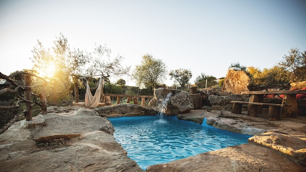 A natural pool surrounded by rocks and trees, with a wooden deck and a stone wall in the background. - Casa Rural Orgullo Rural 4 estrellas (Bermellar)