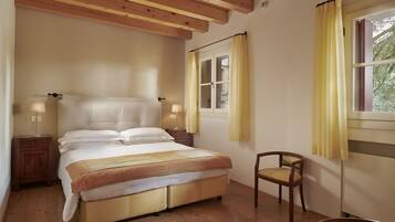 A bedroom with a large bed, wooden floor, two bedside tables with lamps, a chair, and a window with curtains.