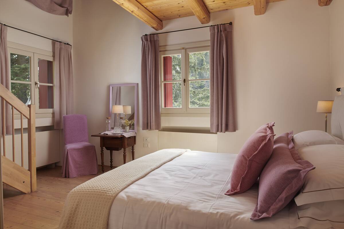 Ein Schlafzimmer mit Bett, Stuhl, Schreibtisch, Fenster mit Vorhängen und Holzboden.