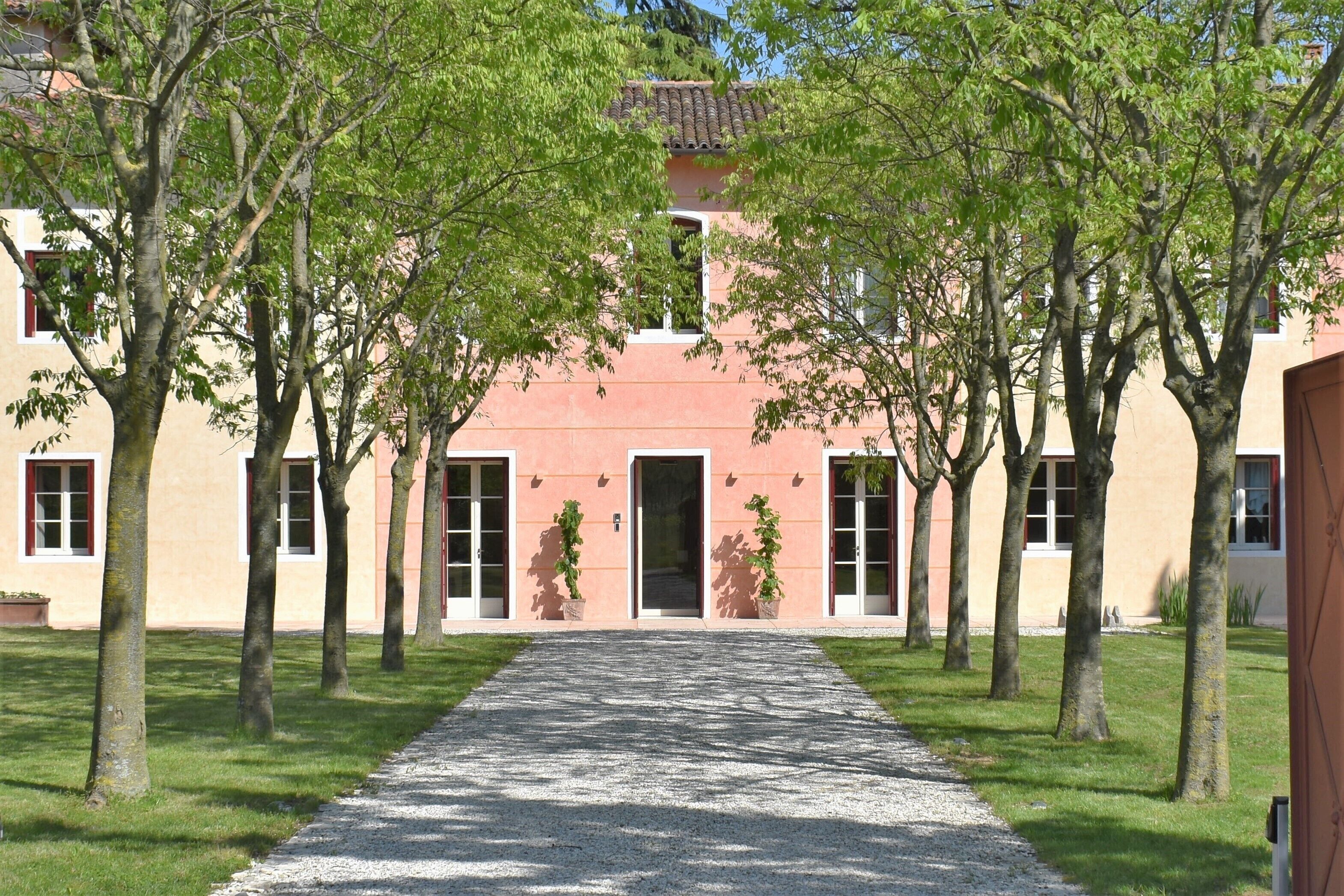 Un edificio con una entrada central, flanqueado por árboles y un camino de grava que conduce hacia él.