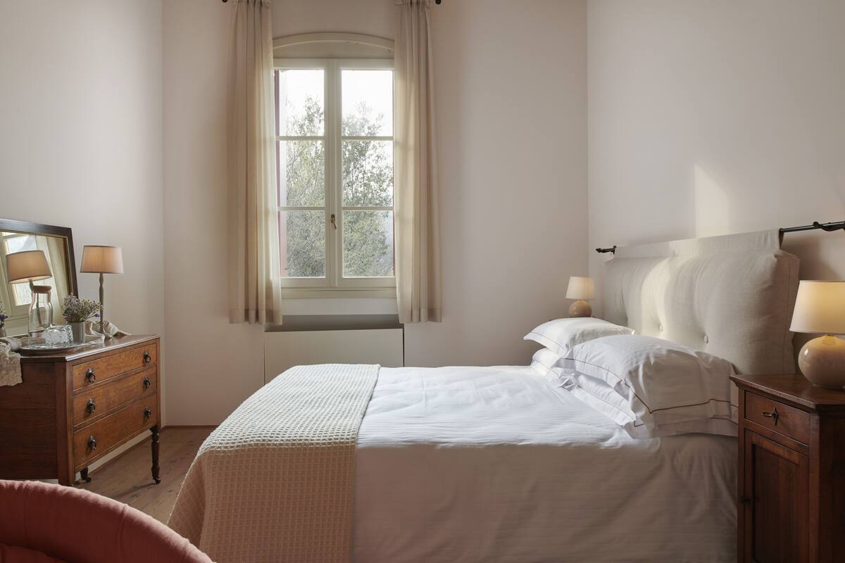 Ein Schlafzimmer mit Bett, Kommode, Spiegel und einem Fenster mit Vorhängen.
