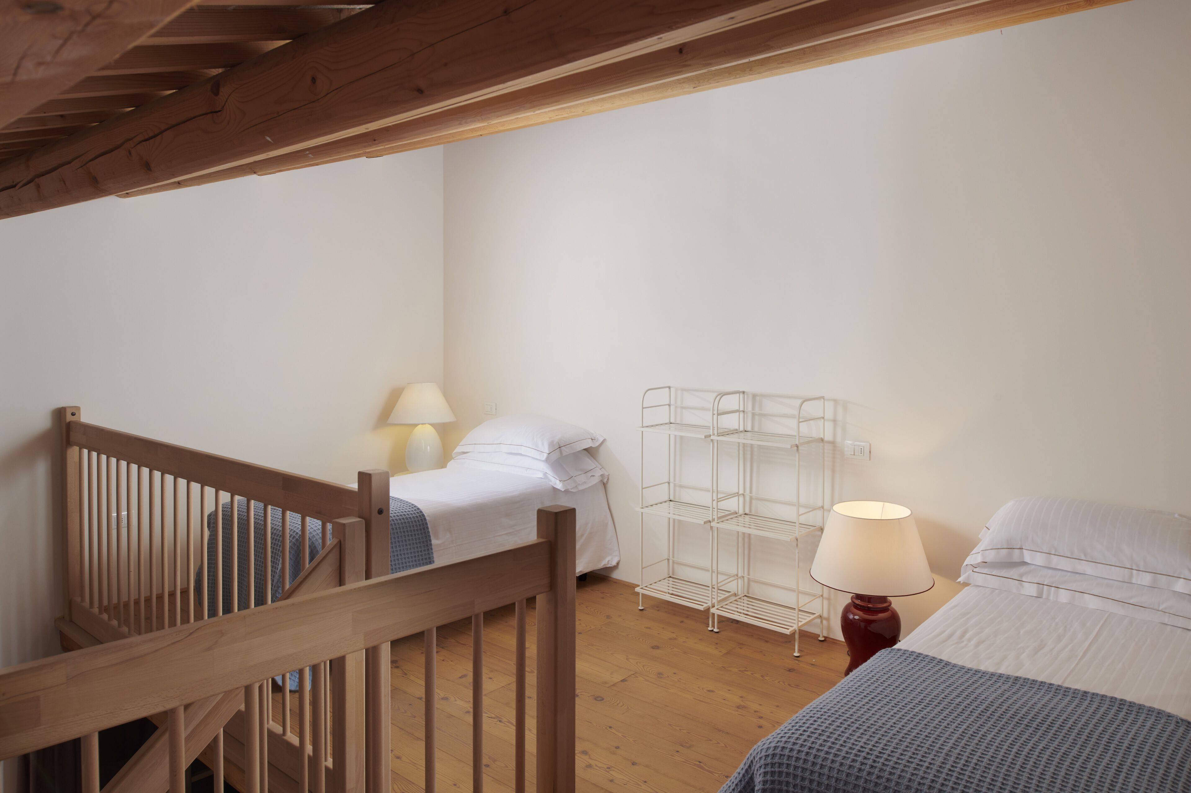 Une chambre avec un escalier en bois, deux lits, une étagère en métal et une lampe.