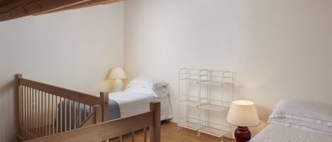 Une chambre avec un escalier en bois, deux lits, une étagère en métal et une lampe.