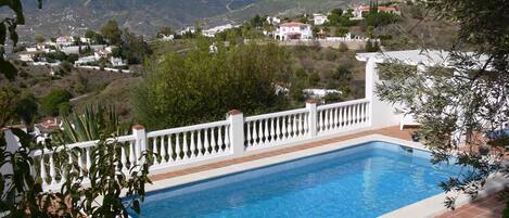 Una piscina con ringhiera bianca, circondata dal verde e con vista su un borgo collinare.