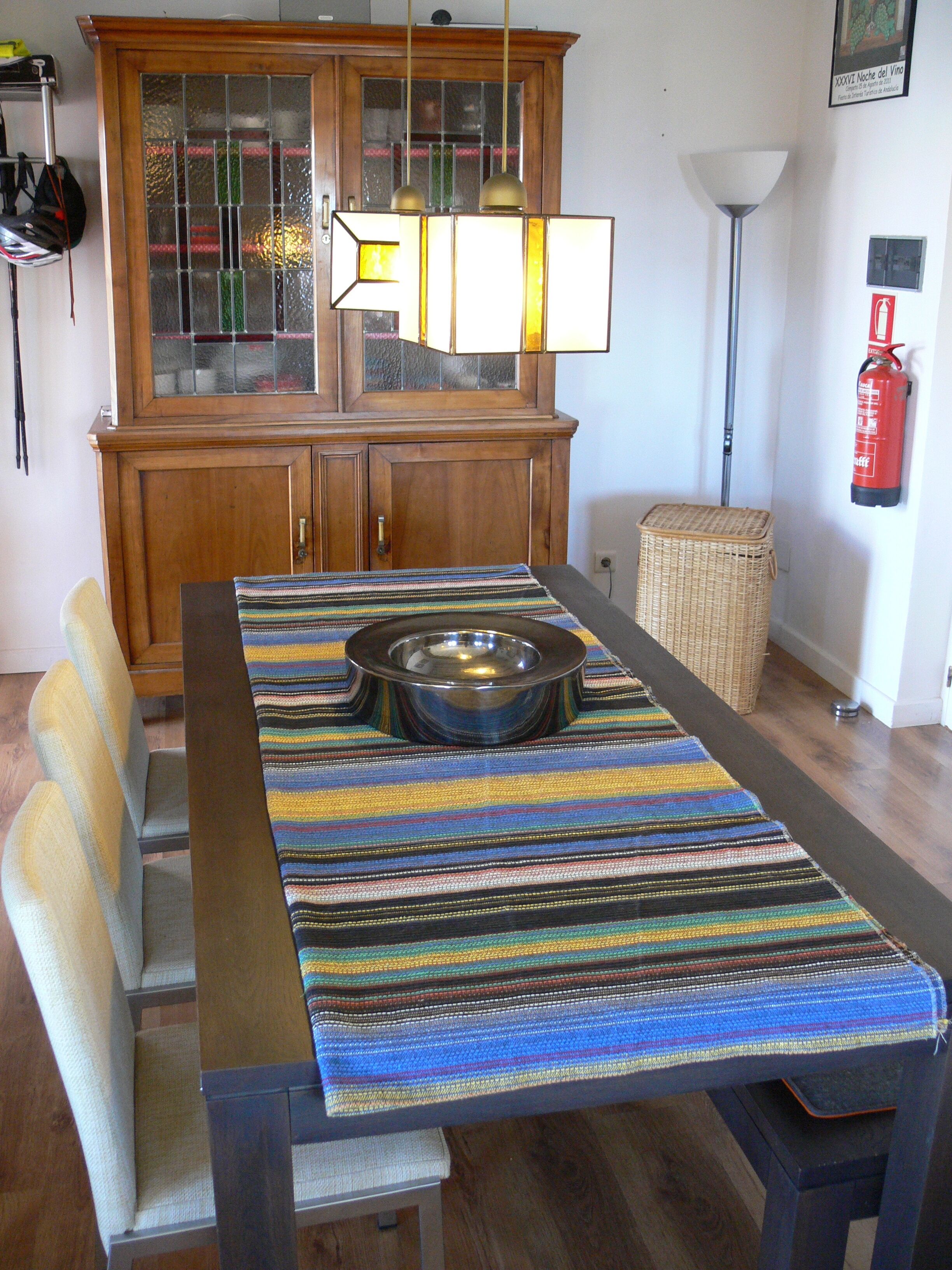 A dining area with a wooden cabinet, a striped tablecloth, a metal bowl, and a wicker basket.