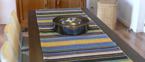 A dining area with a wooden cabinet, a striped tablecloth, a metal bowl, and a wicker basket.