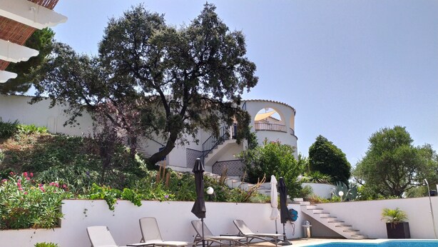 A swimming pool with lounge chairs, a potted plant, and a building with a white facade and arched windows in the background. - Bed and Breakfast La Madrugada (Còmpeta)