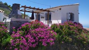 A white building with a stone chimney, a wooden pergola, and a view of the sea. - Bed and Breakfast La Madrugada (Còmpeta)
