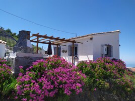 Un edificio blanco con chimenea de piedra, una pérgola de madera y vista al mar.