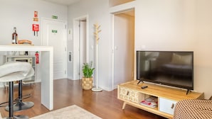 A modern living room with a flat-screen TV, a wooden TV stand, a bar stool, and a potted plant. - Elsas Place, a Home in Madeira (Funchal)
