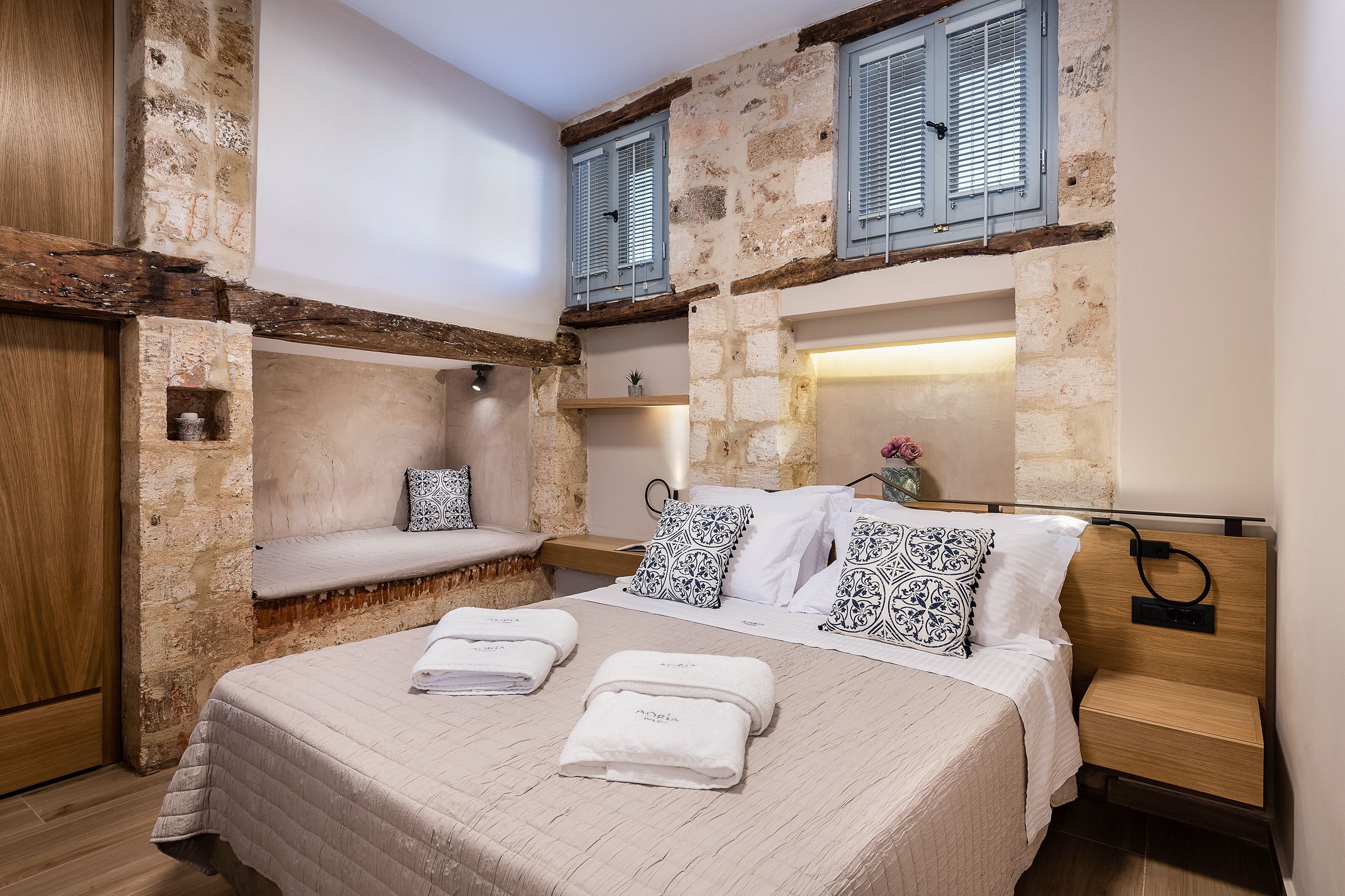 A bedroom with a bed, bedside tables, a bench, and stone walls.