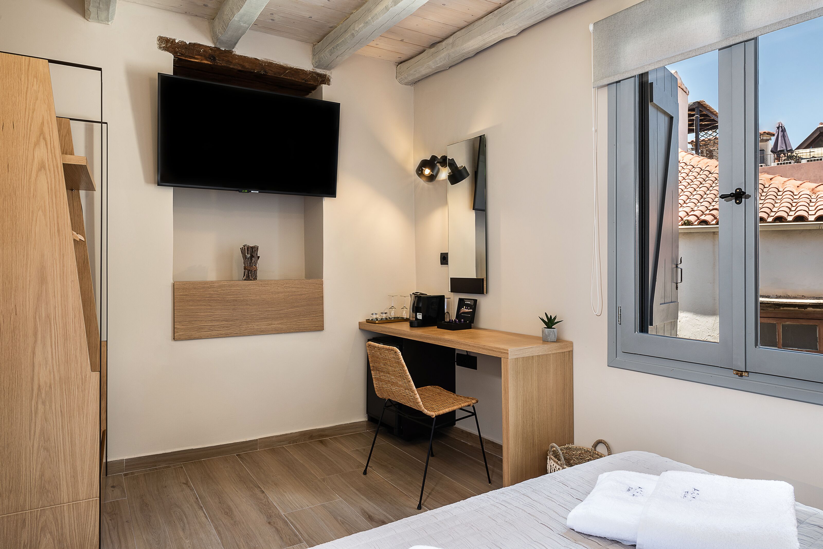 Ein modernes Hotelzimmer mit einem Holztisch, einem Flachbildfernseher, einem großen Spiegel und einem Fenster mit Blick auf Gebäude.