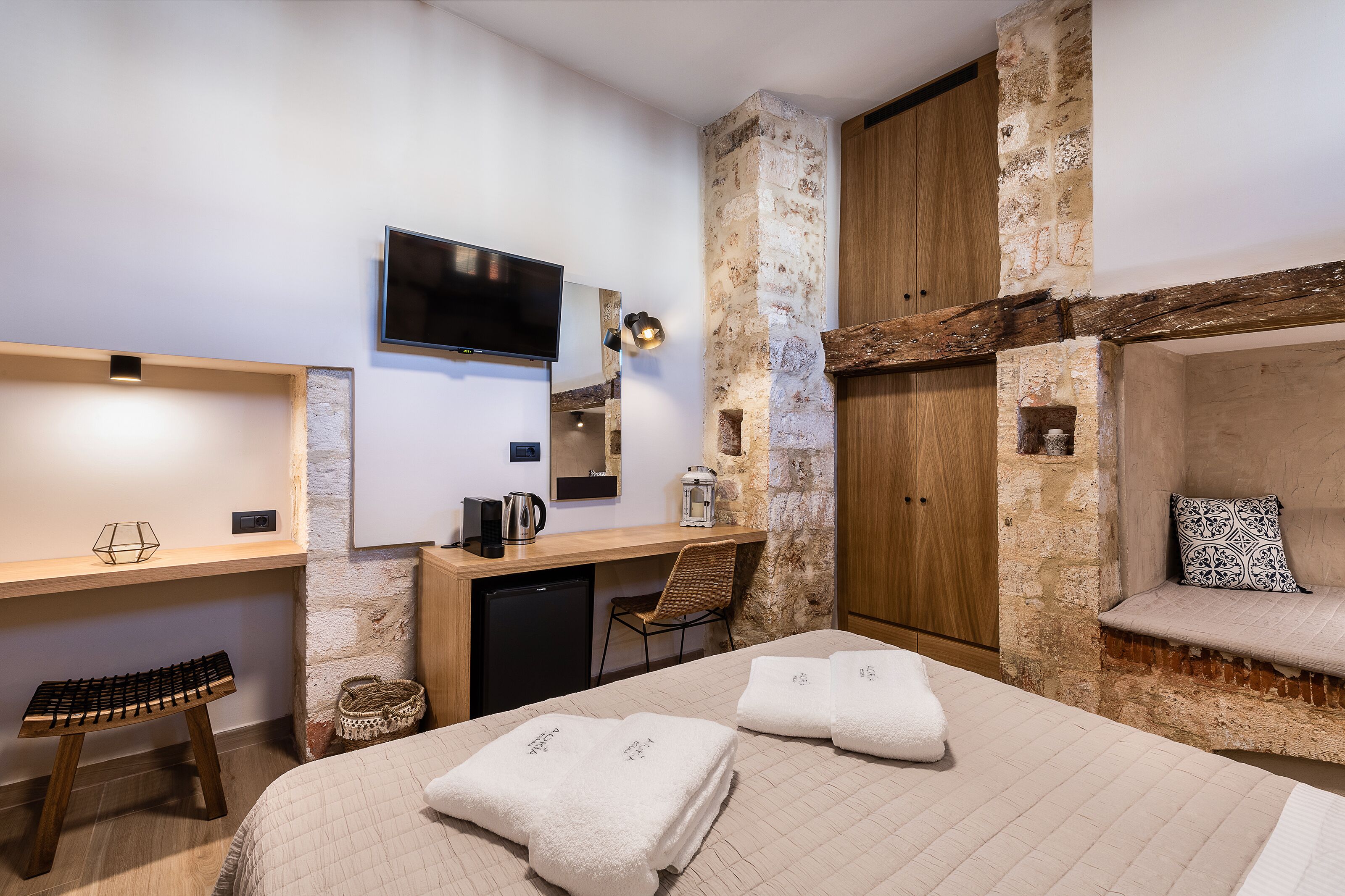 Ein Hotelzimmer mit Bett, Schreibtisch, Fernseher, einer Steinwand und einem Holzschrank.