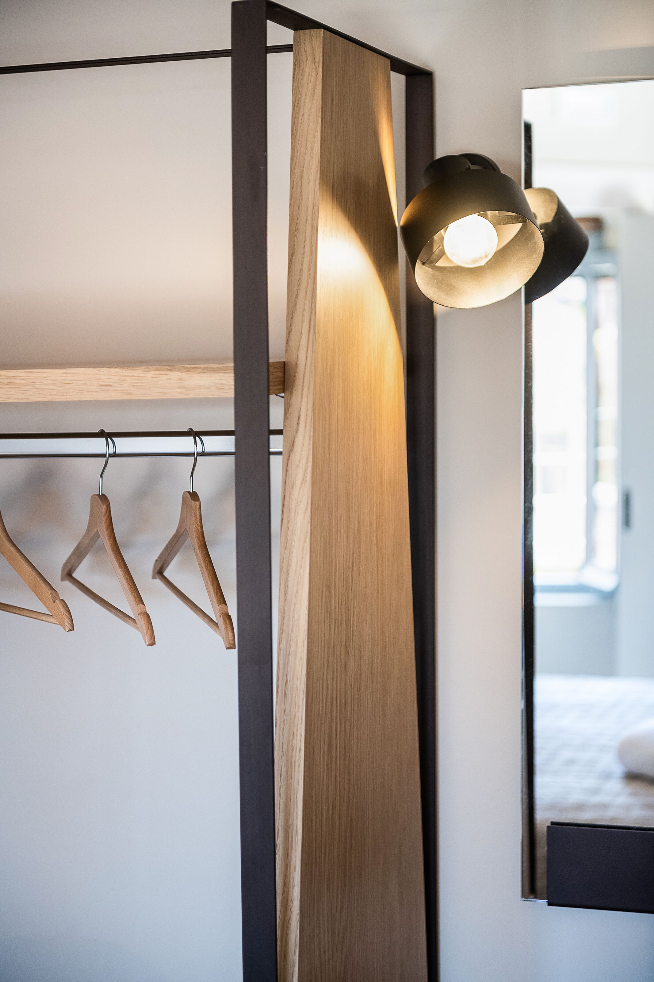 A modern room with a wooden wardrobe, a hanging light fixture, and a mirror reflecting a bed.