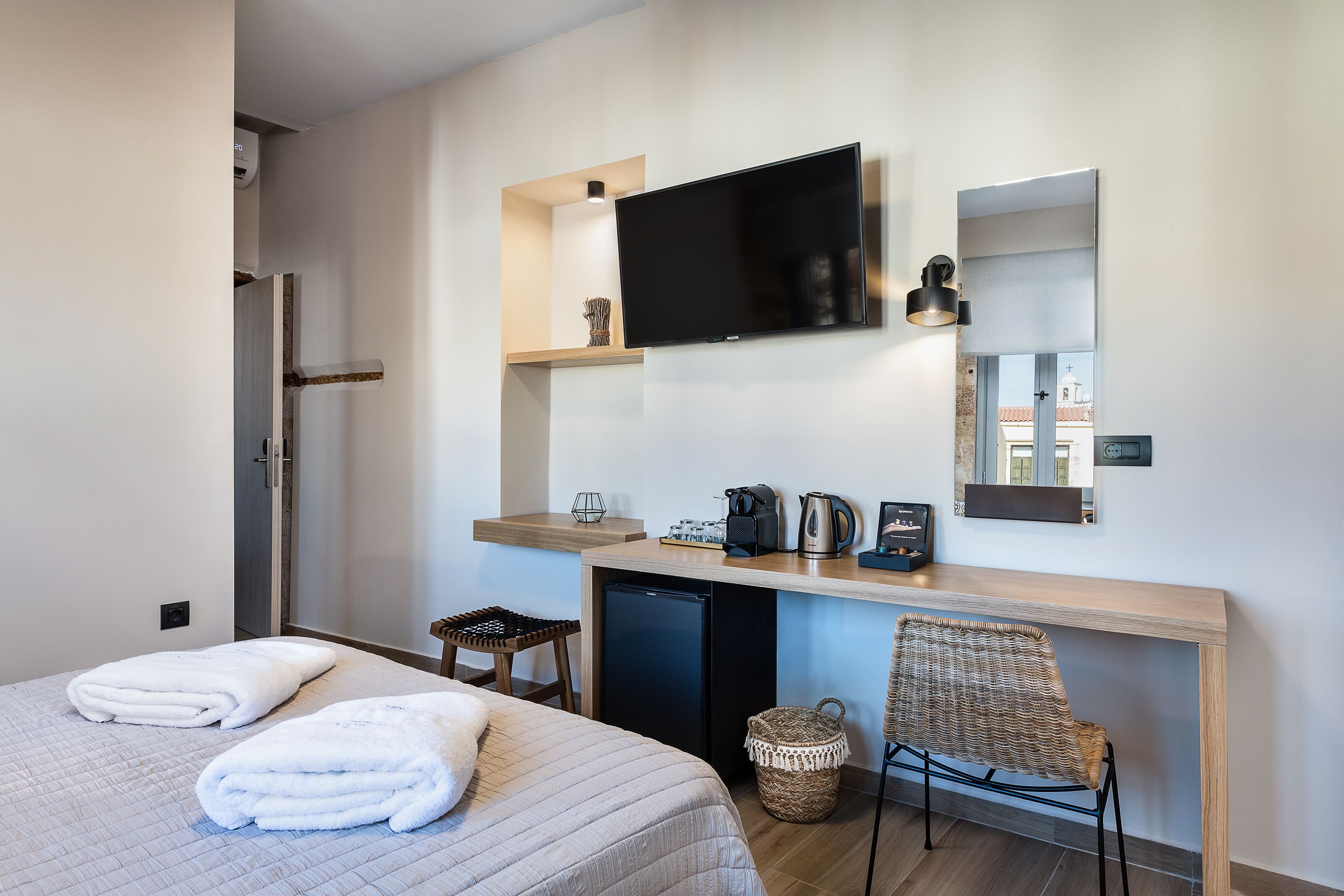 A modern hotel room with a bed, a desk, a TV, and a small kitchenette.