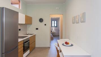 A compact kitchen with a refrigerator, stove, and sink. There is a dining table with chairs and a clock on the wall.