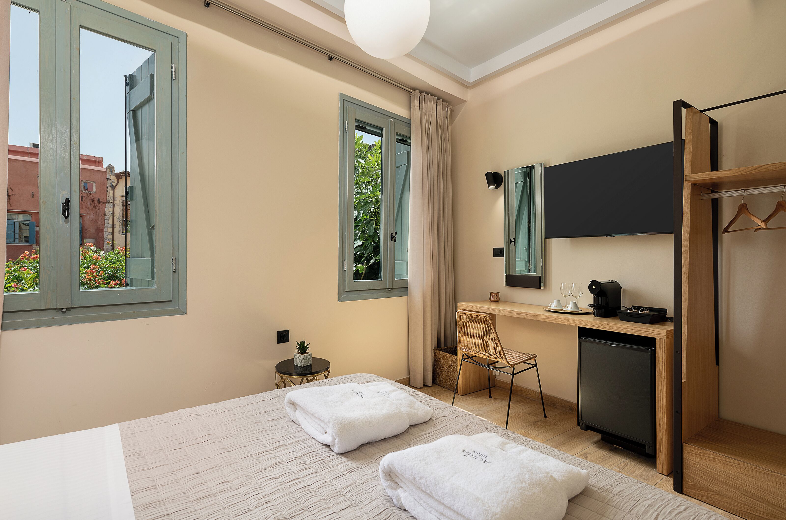 A hotel room with a bed, a desk, a small refrigerator, a chair, and a wardrobe.