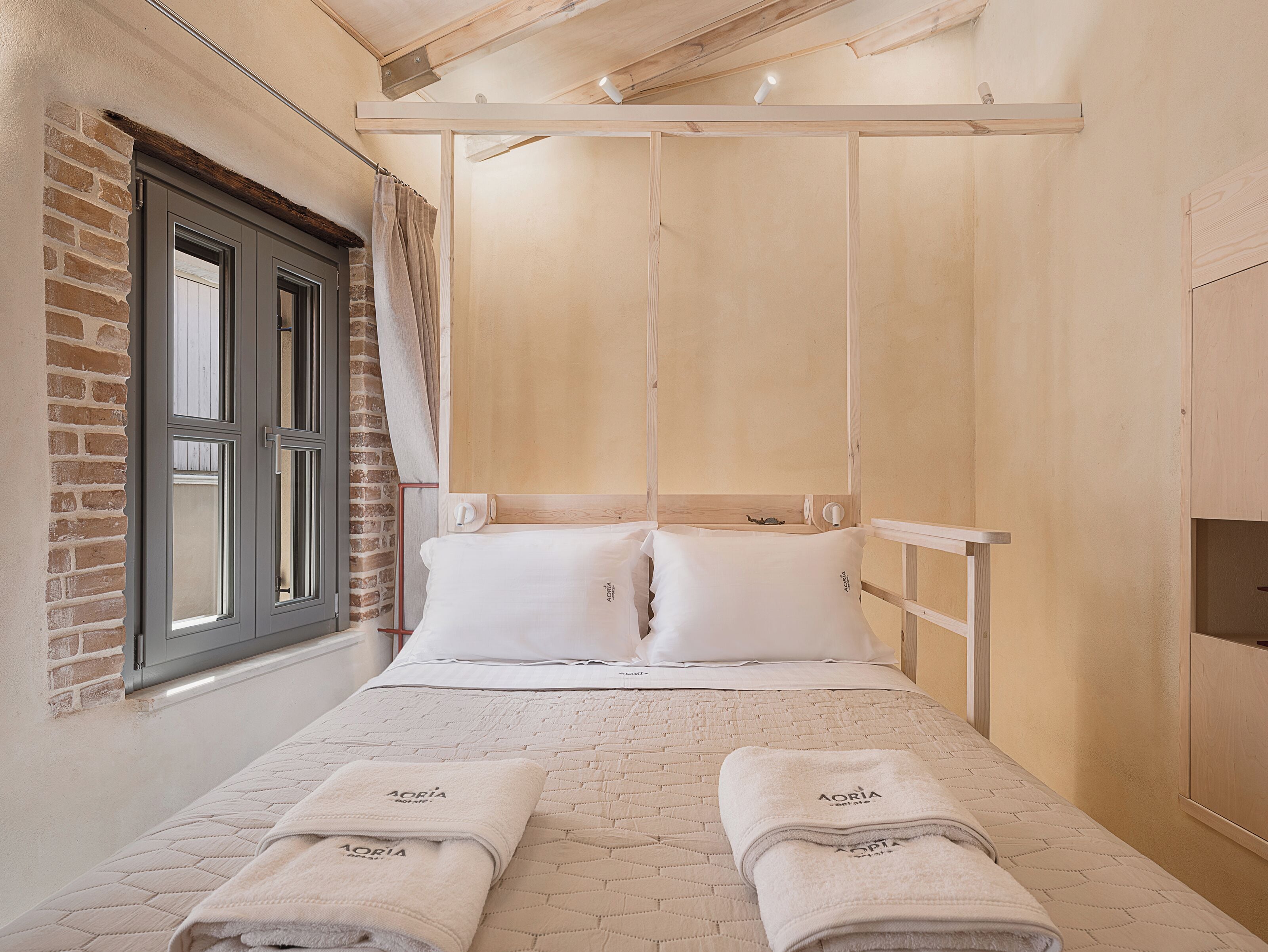 A room with a bed, two pillows, a window with curtains, and a brick wall.