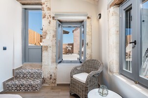 Un pasillo estrecho con una silla de mimbre y una mesita, que conduce a un patio al aire libre.