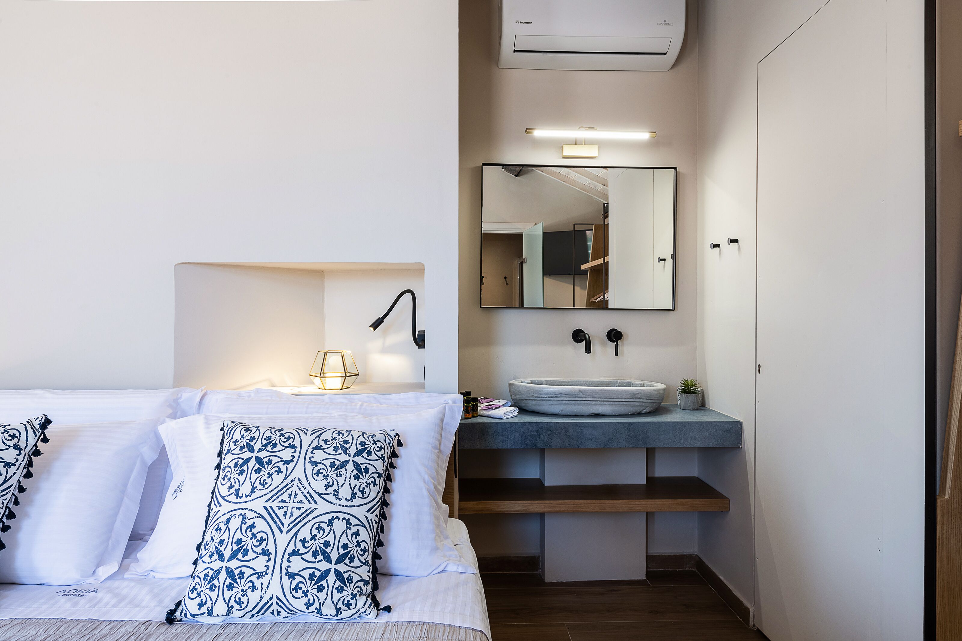 A modern bedroom with a bed, bedside table, and a built-in sink with a mirror above it.